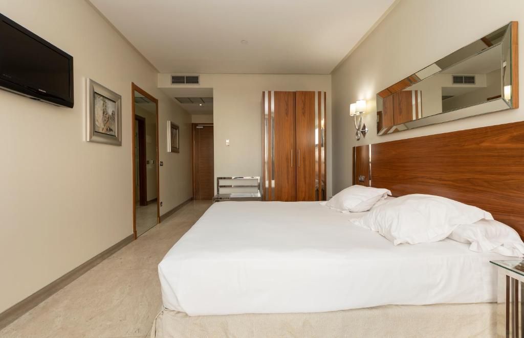 Habitación de hotel con una cama grande, un televisor de pantalla plana montado en la pared, un armario de madera y un espejo sobre la cama.