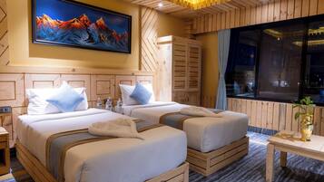 A hotel room with two beds, a large painting of mountains, wooden paneling, and a large window.