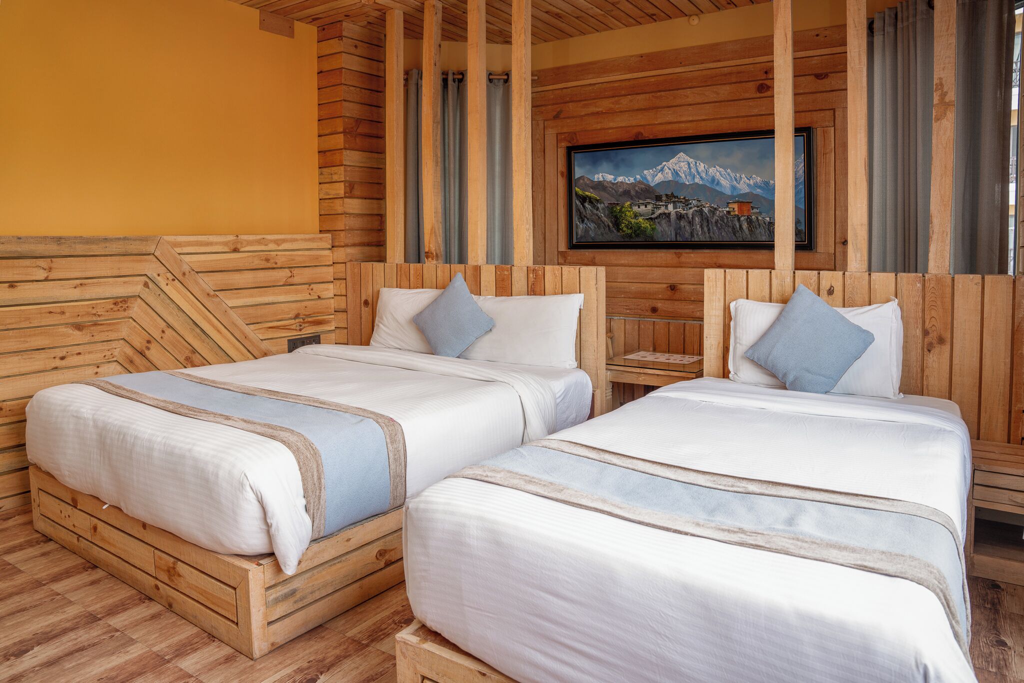 A wooden cabin-style room with two beds, a wooden headboard, a painting of mountains, and a small table.