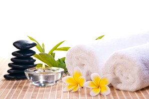 A spa setting with a stack of black stones, a lit candle, white towels, and yellow and white flowers.