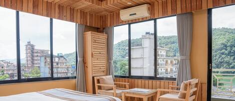 A hotel room with a bed, wooden furniture, large windows, and an air conditioning unit.