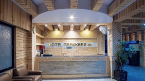 Zona de recepción con un cartel que dice “HOTEL TREKKERS INN”, paneles de madera, mostrador de recepción, un reloj y un área de estar con un sofá y una mesa de centro.