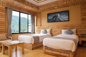 A hotel room with two beds, a wooden headboard, a large window with a view of a mountain, and a painting on the wall.