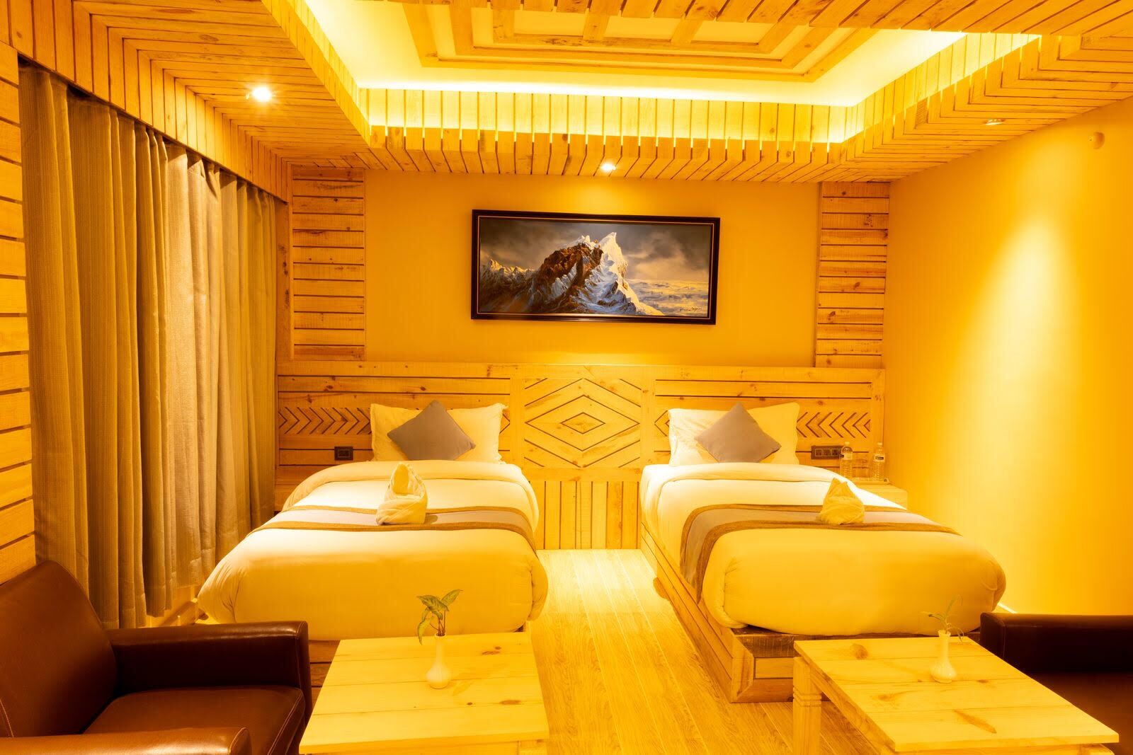 A hotel room with two beds, wooden paneling, a painting on the wall, and a small plant on the nightstand.