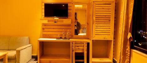 Una habitación con un mueble bajo de madera para el televisor, un sofá, un escritorio con espejo y una ventana con cortinas.