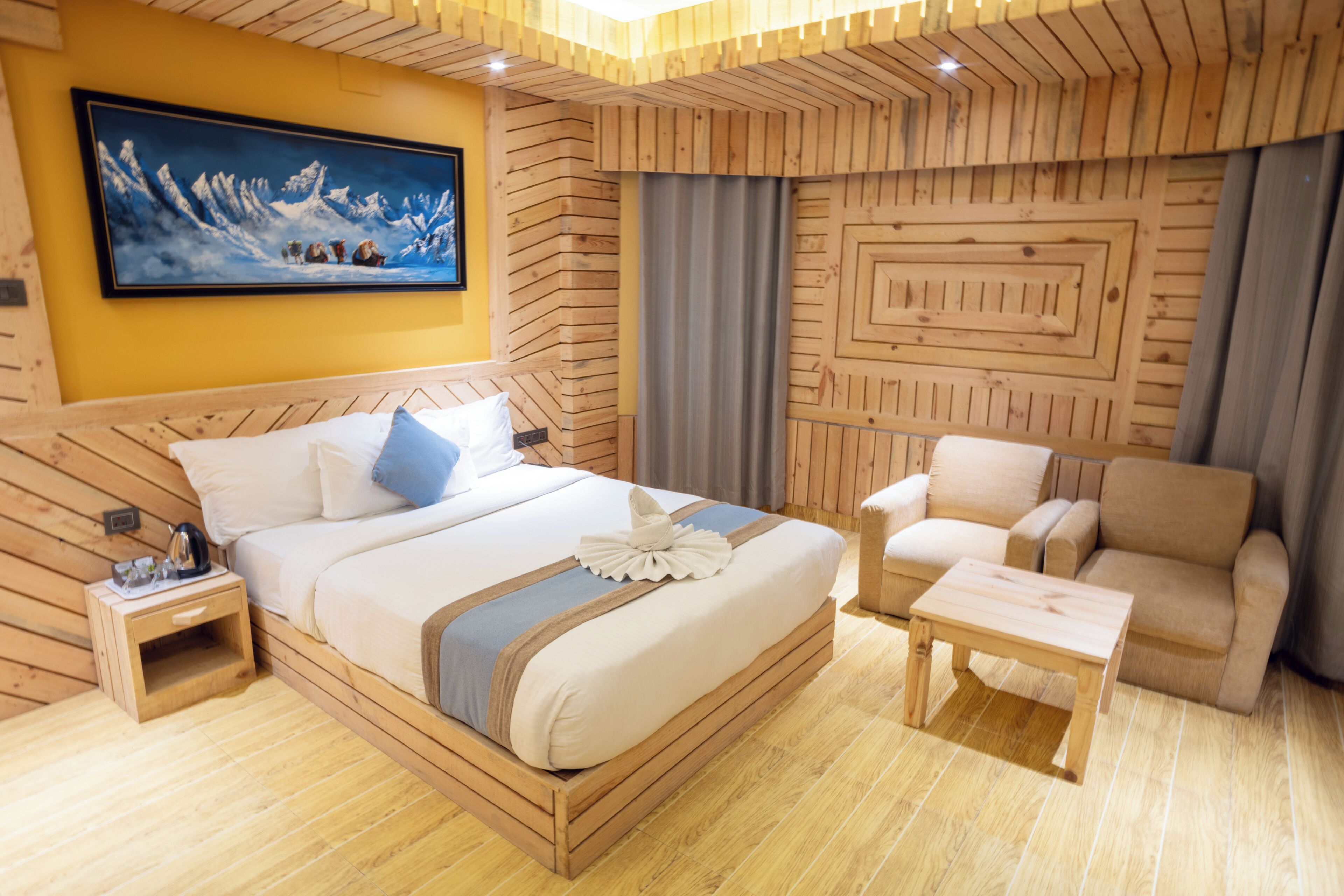 Habitación de hotel con decoración de madera, con una cama grande, un sofá, una mesita y un cuadro en la pared.