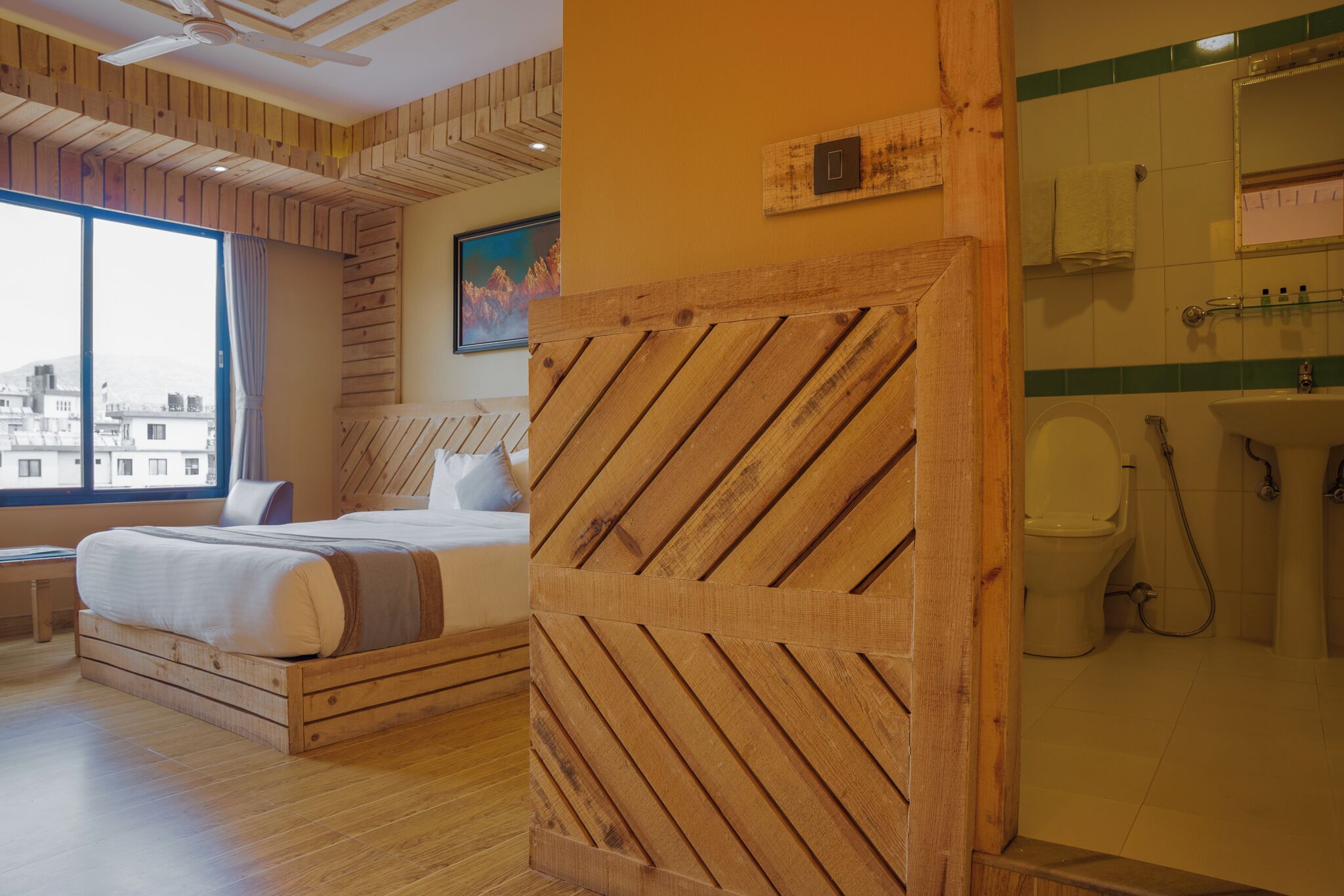 A hotel room with a wooden headboard, a bed, a window with a view, and a bathroom with a toilet and sink.