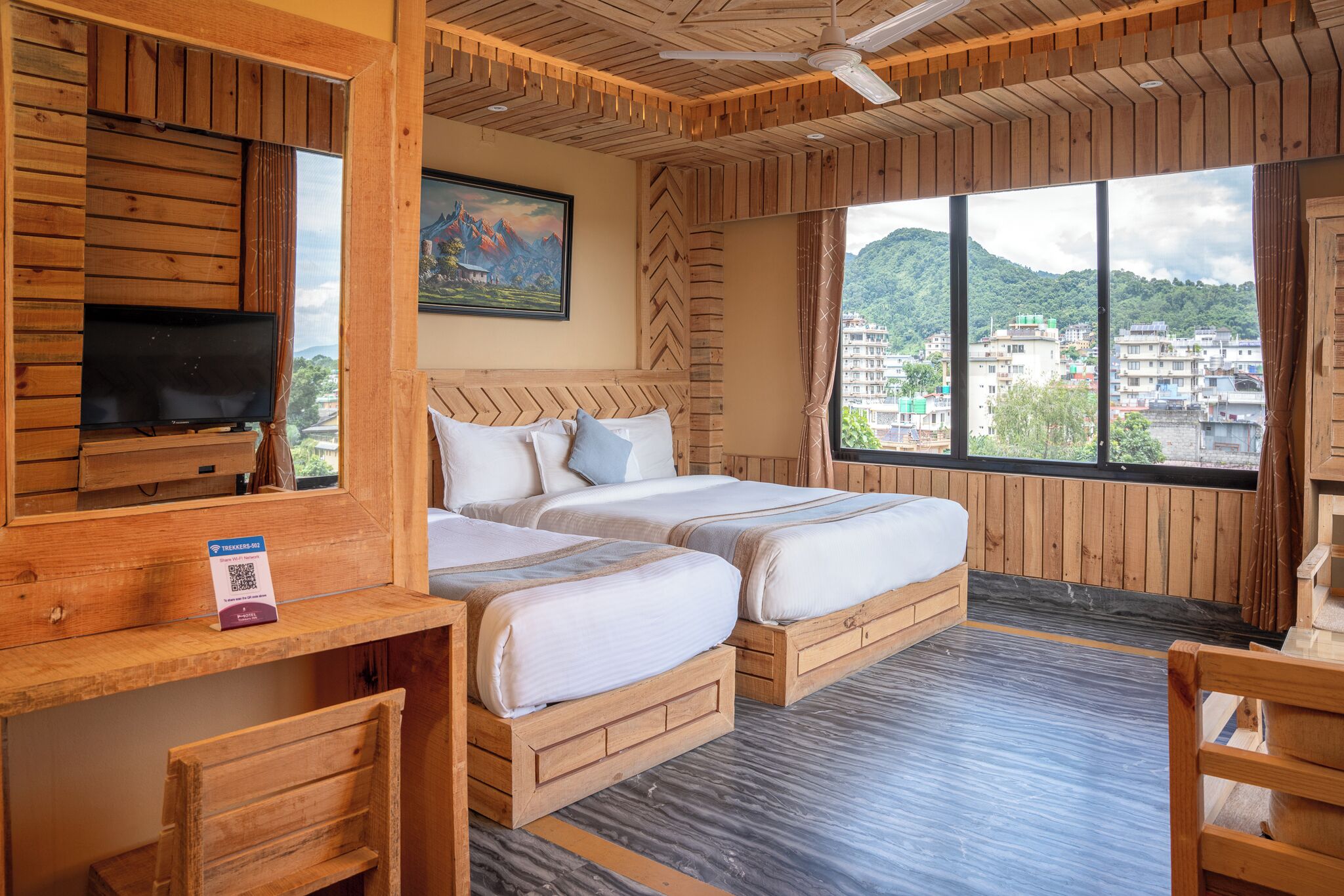 A wooden-themed hotel room with two beds, a TV, and a desk.