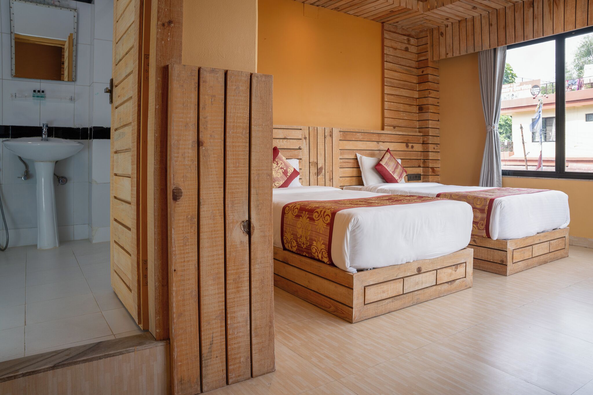 A room with two wooden beds, a sink, and a window with a view of buildings outside.