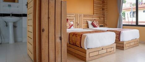A room with two wooden beds, a sink, and a window with a view of buildings outside.