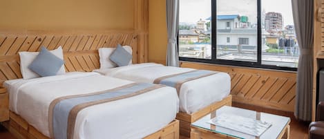 Una habitación con dos camas de madera, una mesa de vidrio y vistas a edificios a través de un amplio ventanal.