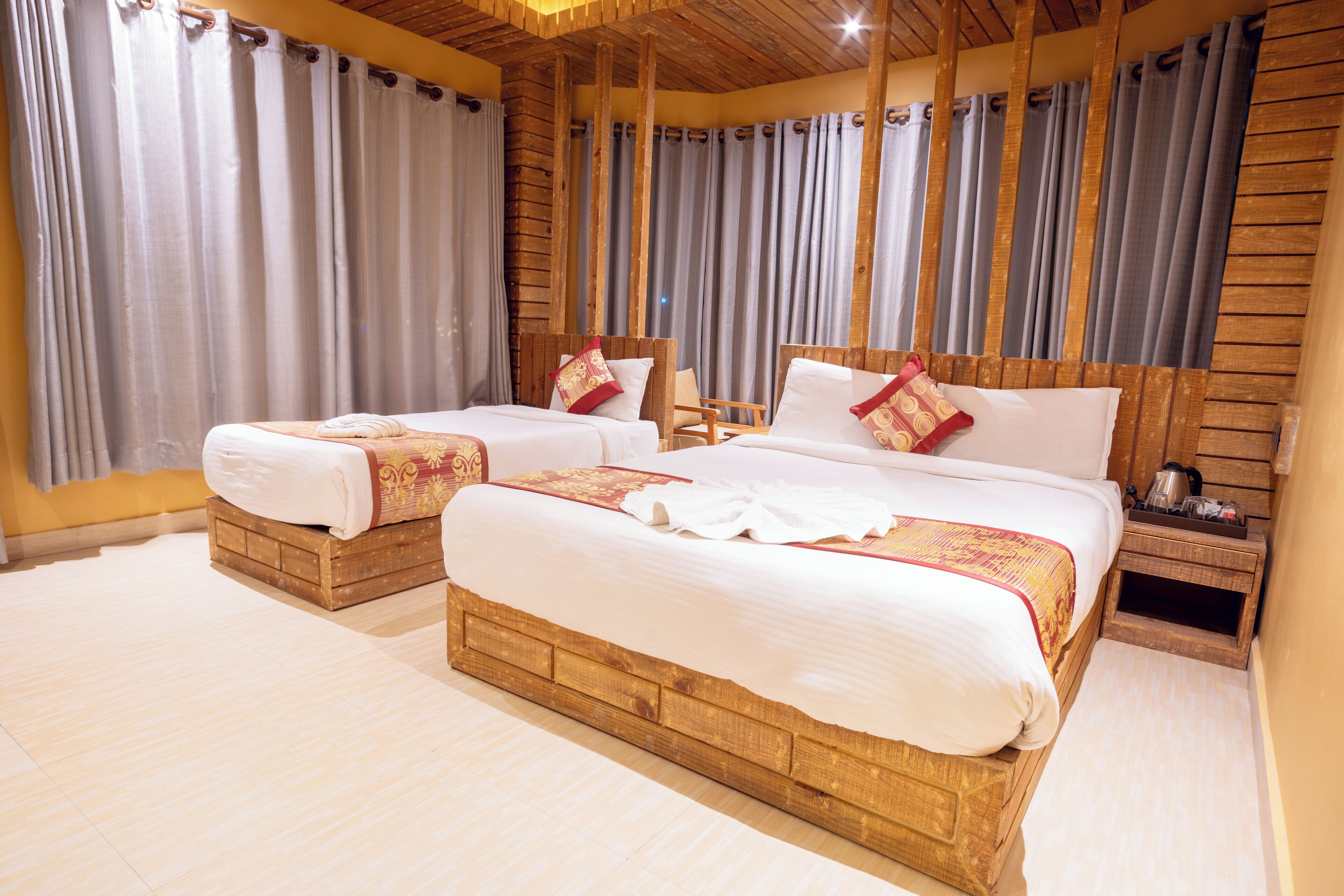 A hotel room with two wooden beds, a wooden headboard, a small wooden nightstand, and a large window with curtains.