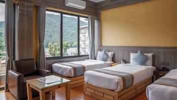 A hotel room with two beds, a sofa, a small table, and a large window offering a mountain view.