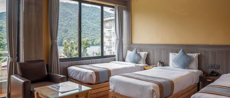 A hotel room with two beds, a sofa, a small table, and a large window offering a mountain view.