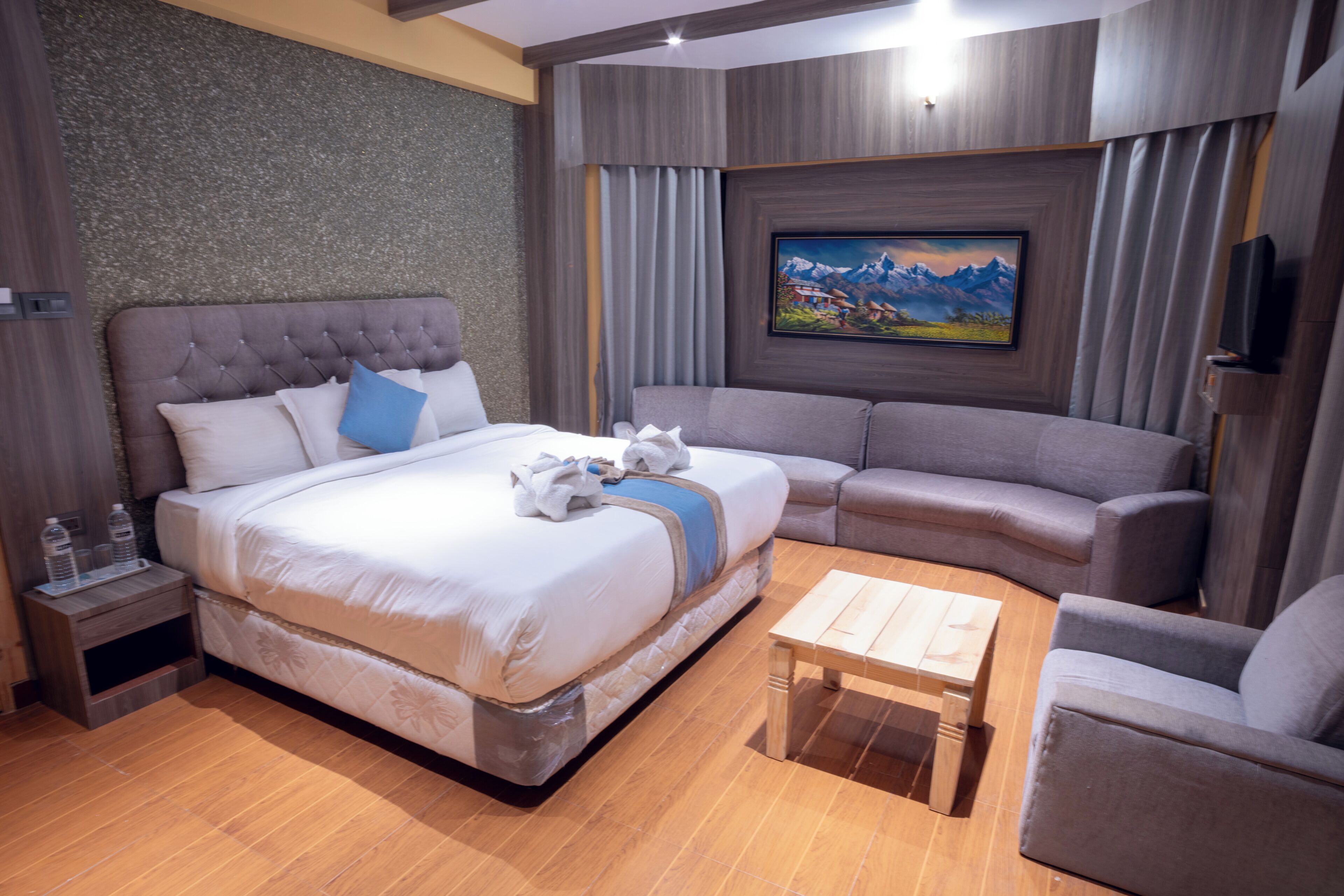 A modern hotel room with a large bed, a sofa, a small table, and a painting on the wall.