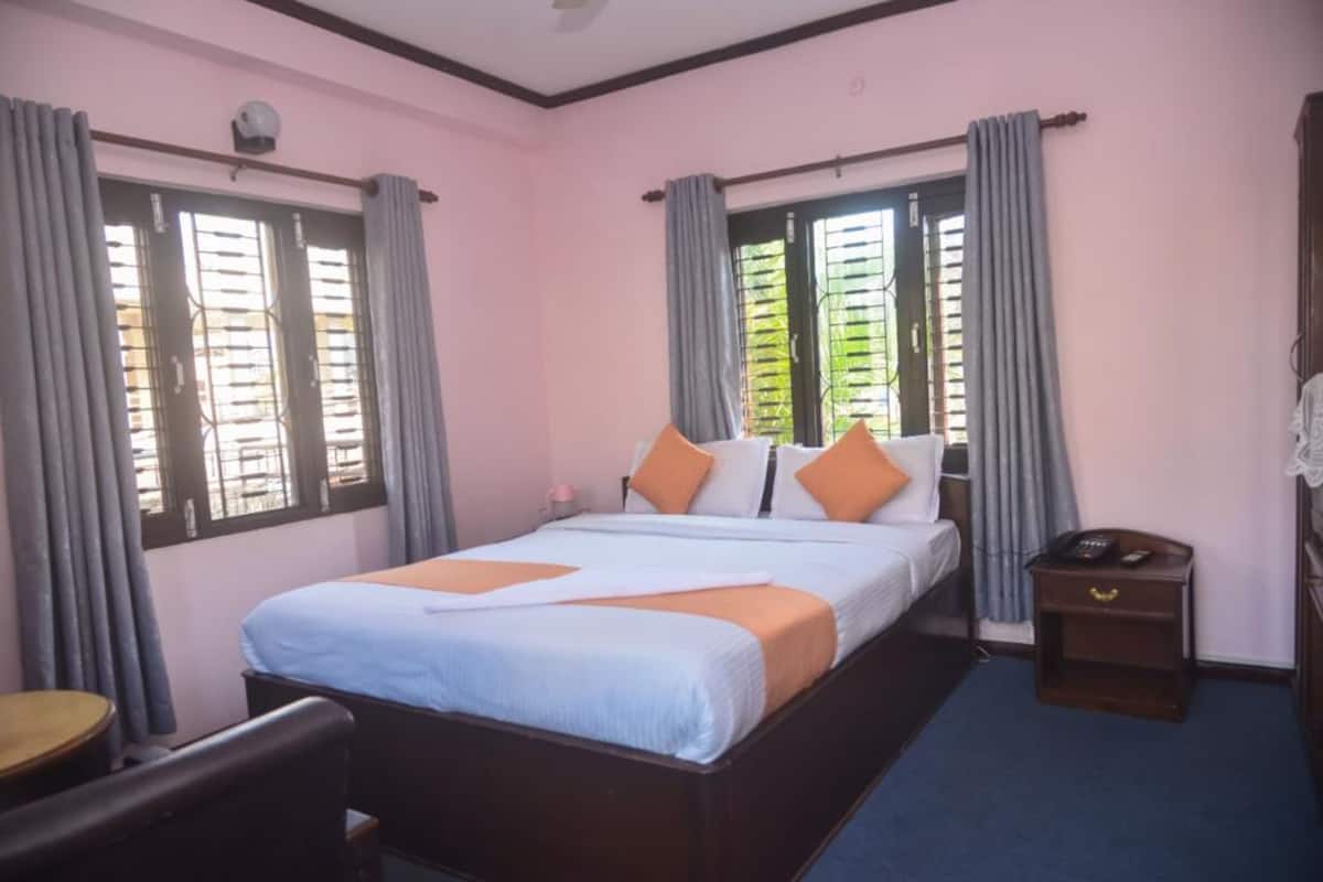 Une chambre d’hôtel avec un lit, une table de chevet, une chaise et une fenêtre avec des rideaux.