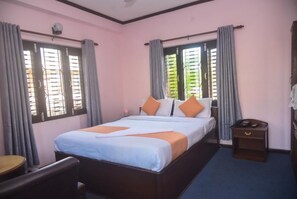 A hotel room with a bed, a bedside table, a chair, and a window with curtains. - Hotel Travel-Inn (Pokhara)