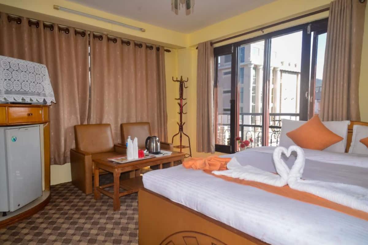 Une chambre d’hôtel avec un lit, un bureau doté d’une bouilloire, un porte-manteau et une vue sur les bâtiments par la fenêtre.
