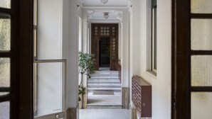 Un pasillo con una escalera de mármol, puertas de madera y una planta en maceta.