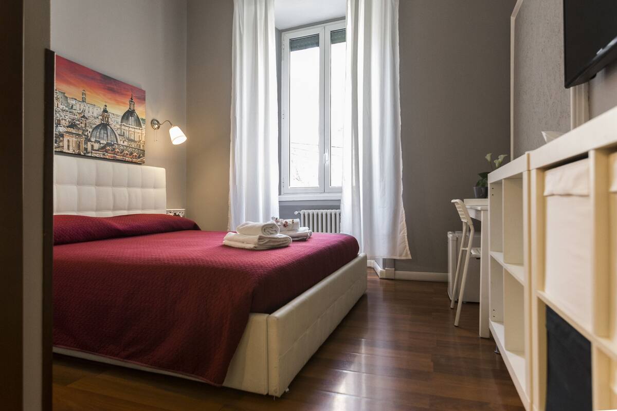 A bedroom with a large bed, a radiator, a desk, and a window with curtains.