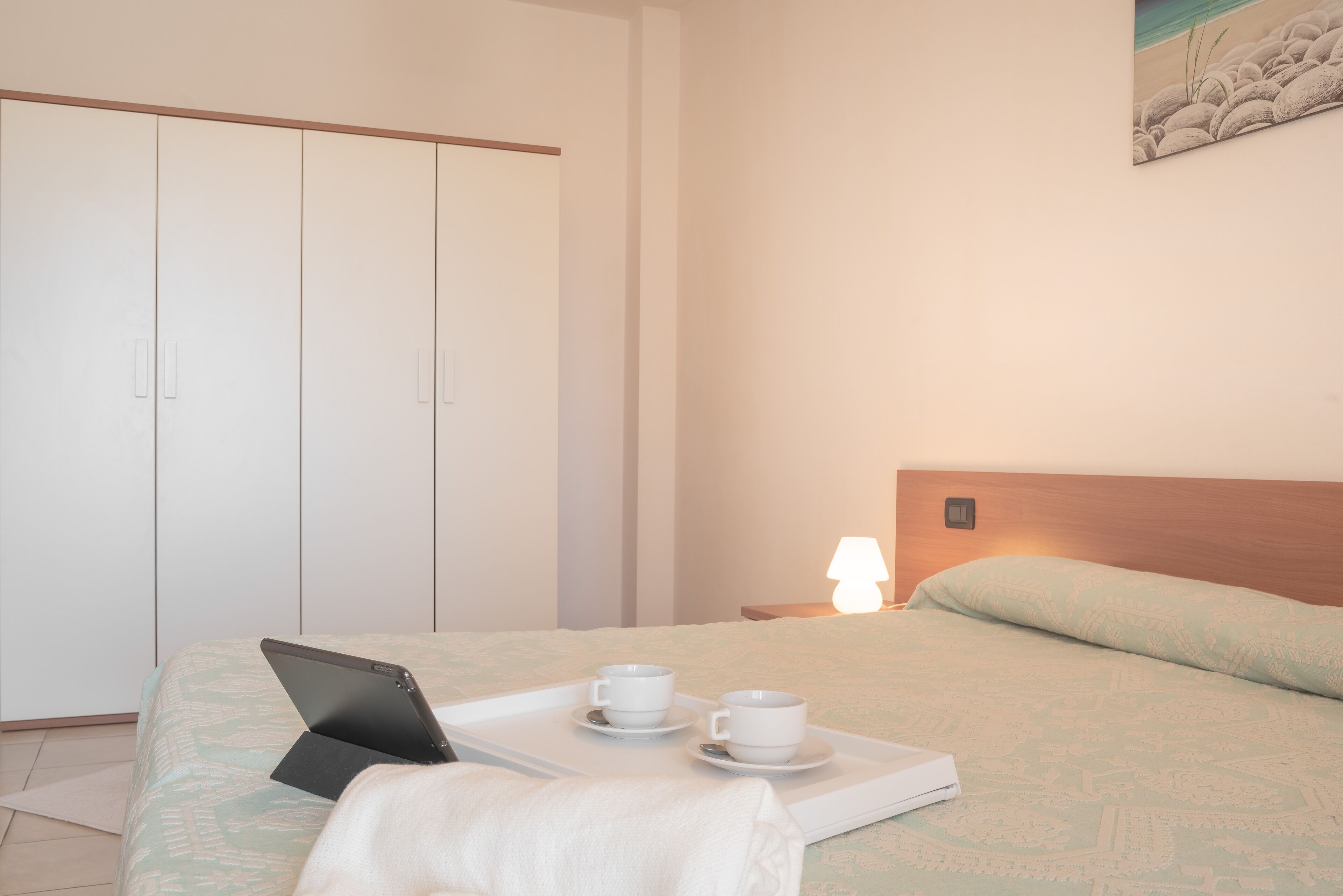 A neatly made bed with a laptop, two cups, and a tray.