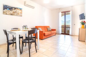 A dining area with a white table and chairs, a sofa, and a balcony with a view. - Residence Le Fontane (Villasimius)
