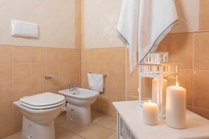 A bathroom with a toilet, bidet, and sink, and three lit candles on the counter. - Residence Le Fontane (Villasimius)