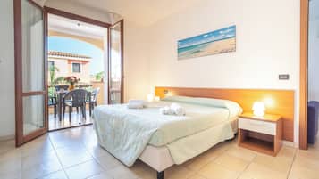 Habitación de hotel con cama, mesita de noche, un cuadro de playa y vistas al exterior.