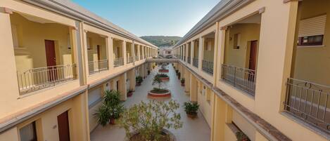 A corridor with balconies, potted plants, and a central walkway.