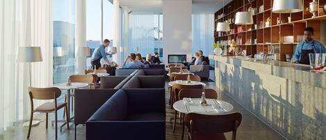 A modern restaurant with high ceilings, large windows, and a bar area.