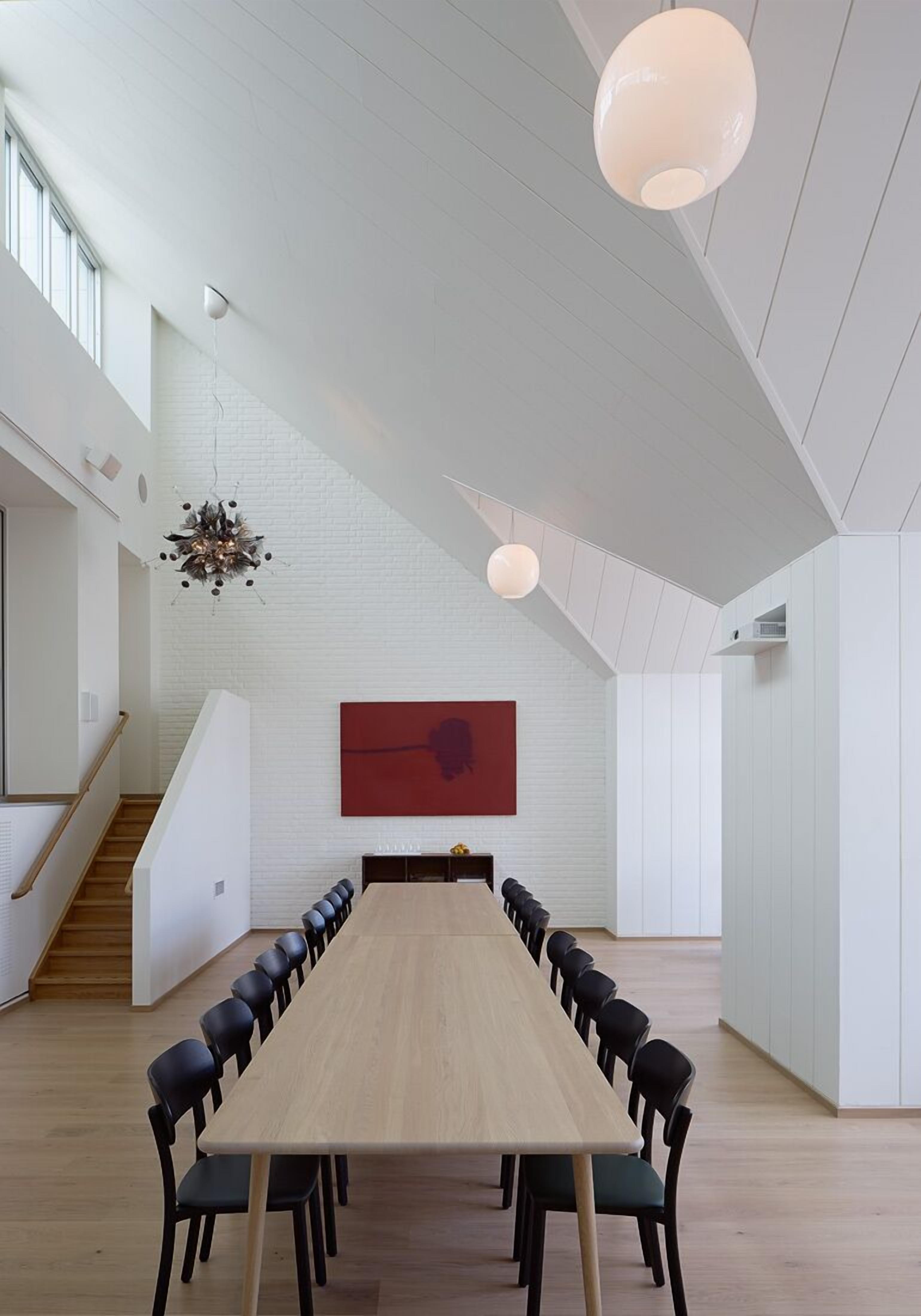 A spacious conference room with a long table and chairs, white walls, and a staircase on the left.