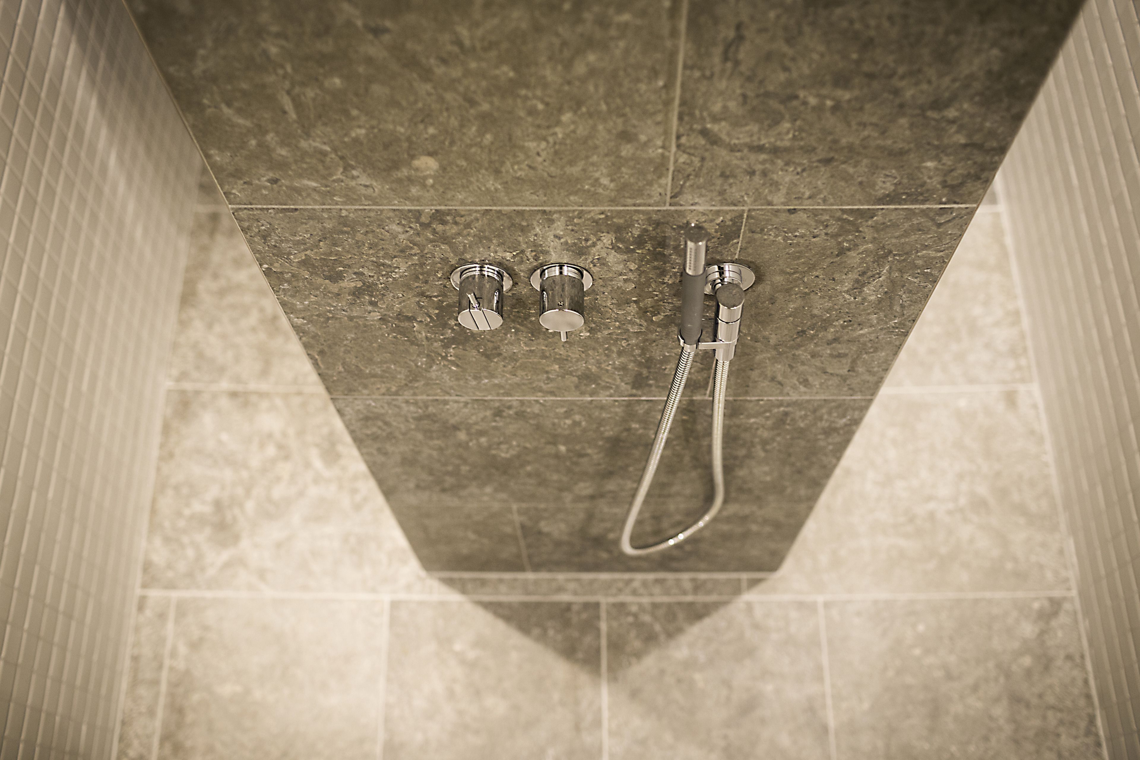 A shower area with a handheld showerhead and two wall-mounted faucets.