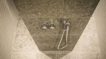 A shower area with a handheld showerhead and two wall-mounted faucets.