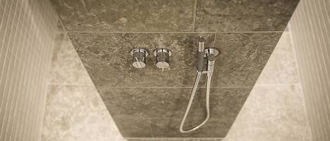 A shower area with a handheld showerhead and two wall-mounted faucets.