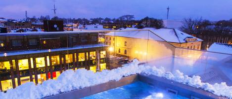 A swimming pool surrounded by snow, with a building in the background.