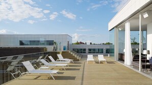 A rooftop terrace with sun loungers and a modern building with large windows. - PM & Vänner Hotel (Växjö)