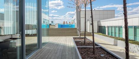 Un edificio moderno con amplios ventanales, una terraza de madera y un cerezo en flor.