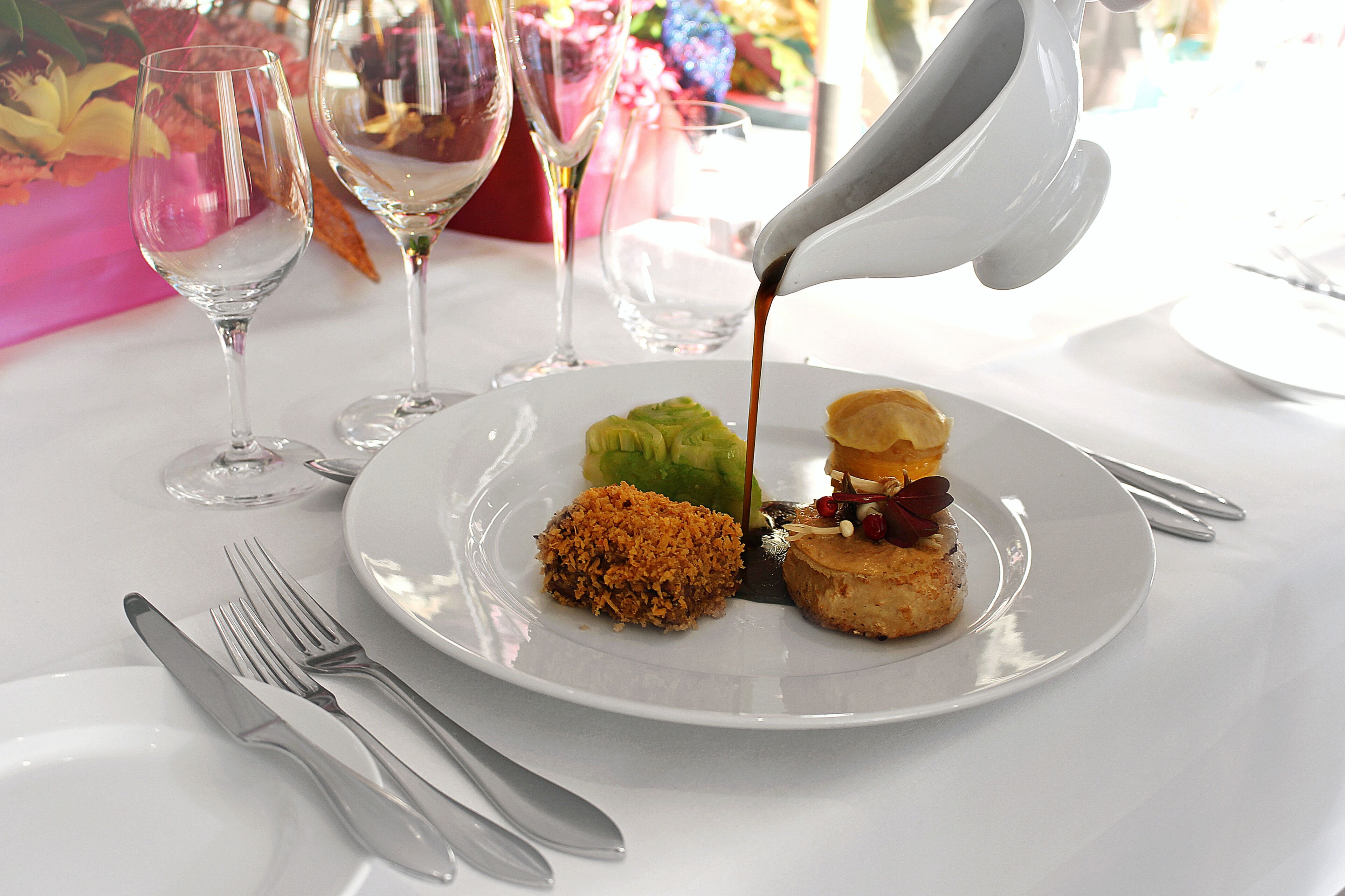 A plate with food and a sauce being poured, accompanied by cutlery and wine glasses.