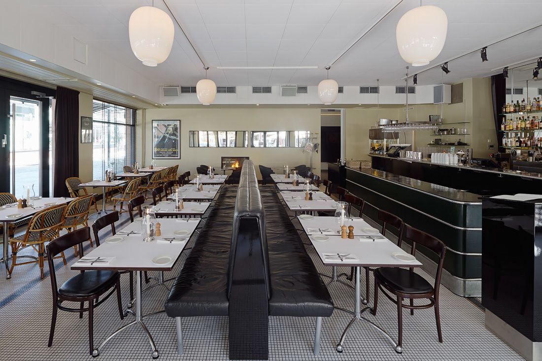 A spacious restaurant with long tables, a central bar, and a view of the city through large windows.
