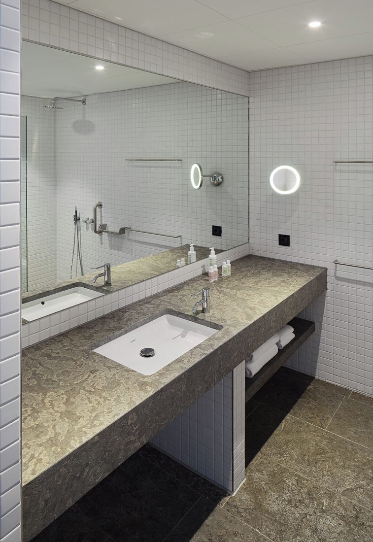 A modern bathroom with a large mirror, two sinks, and a vanity with a marble countertop.