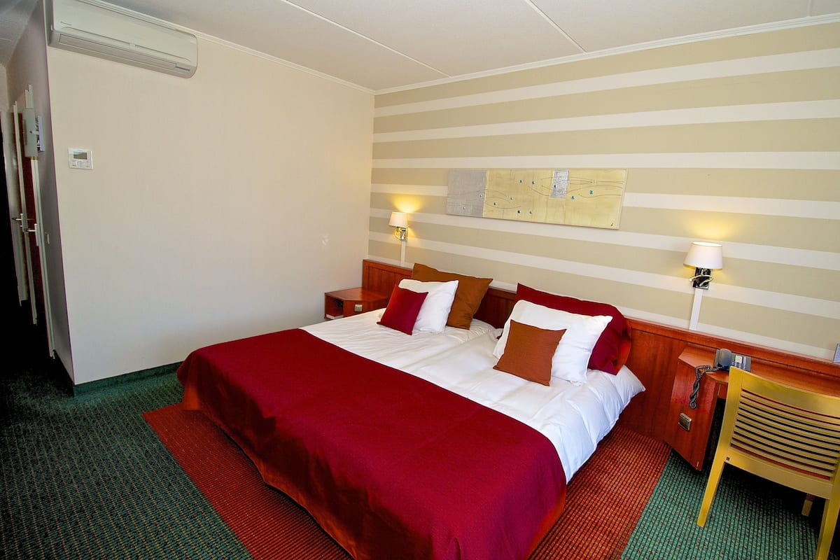 Una habitación de hotel con una cama grande, dos mesitas de noche, un cabecero de madera, un mapa colgado en la pared y dos lámparas de pared.