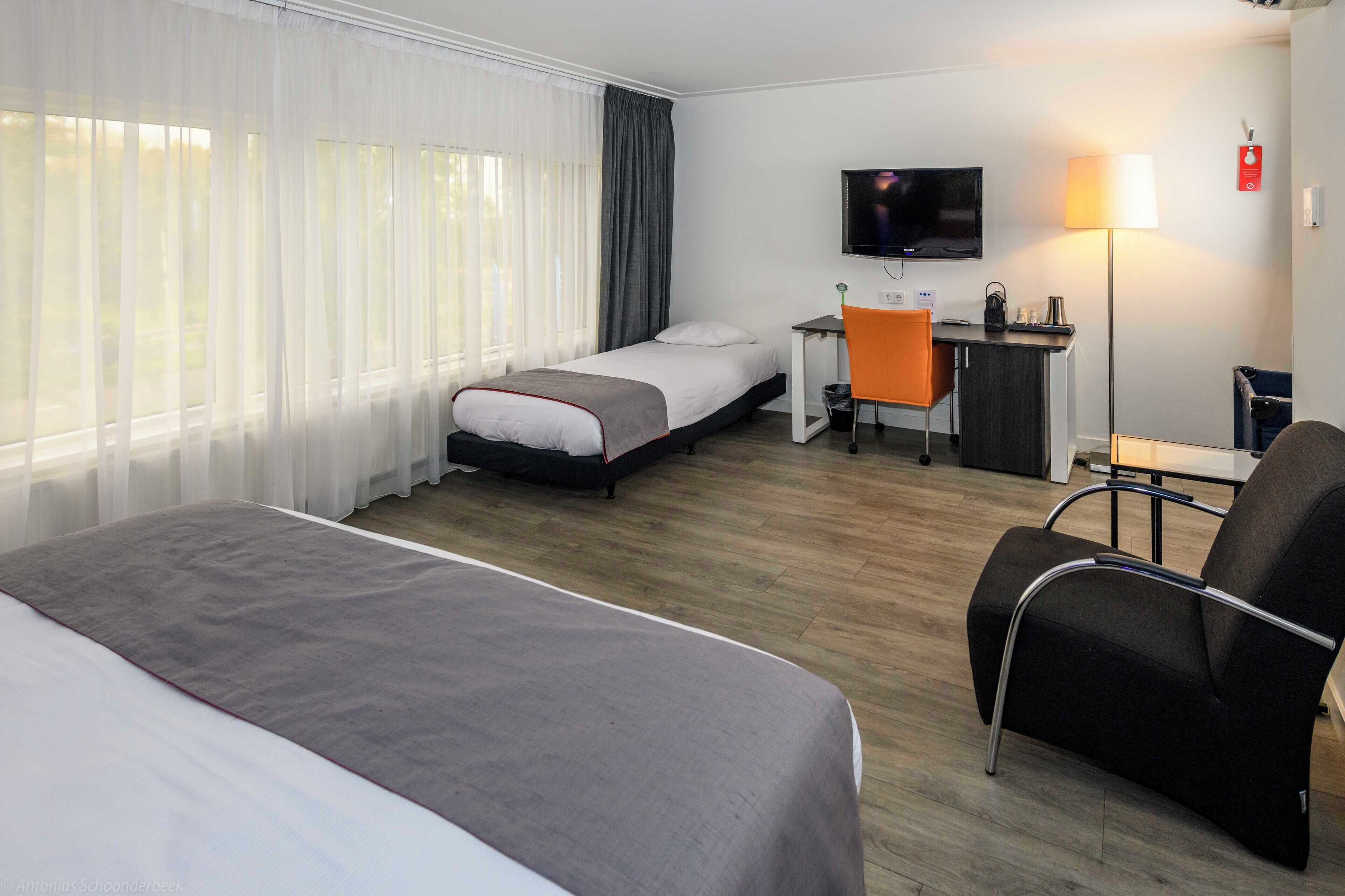 A hotel room with a bed, a desk, a chair, a TV, and a lamp.
