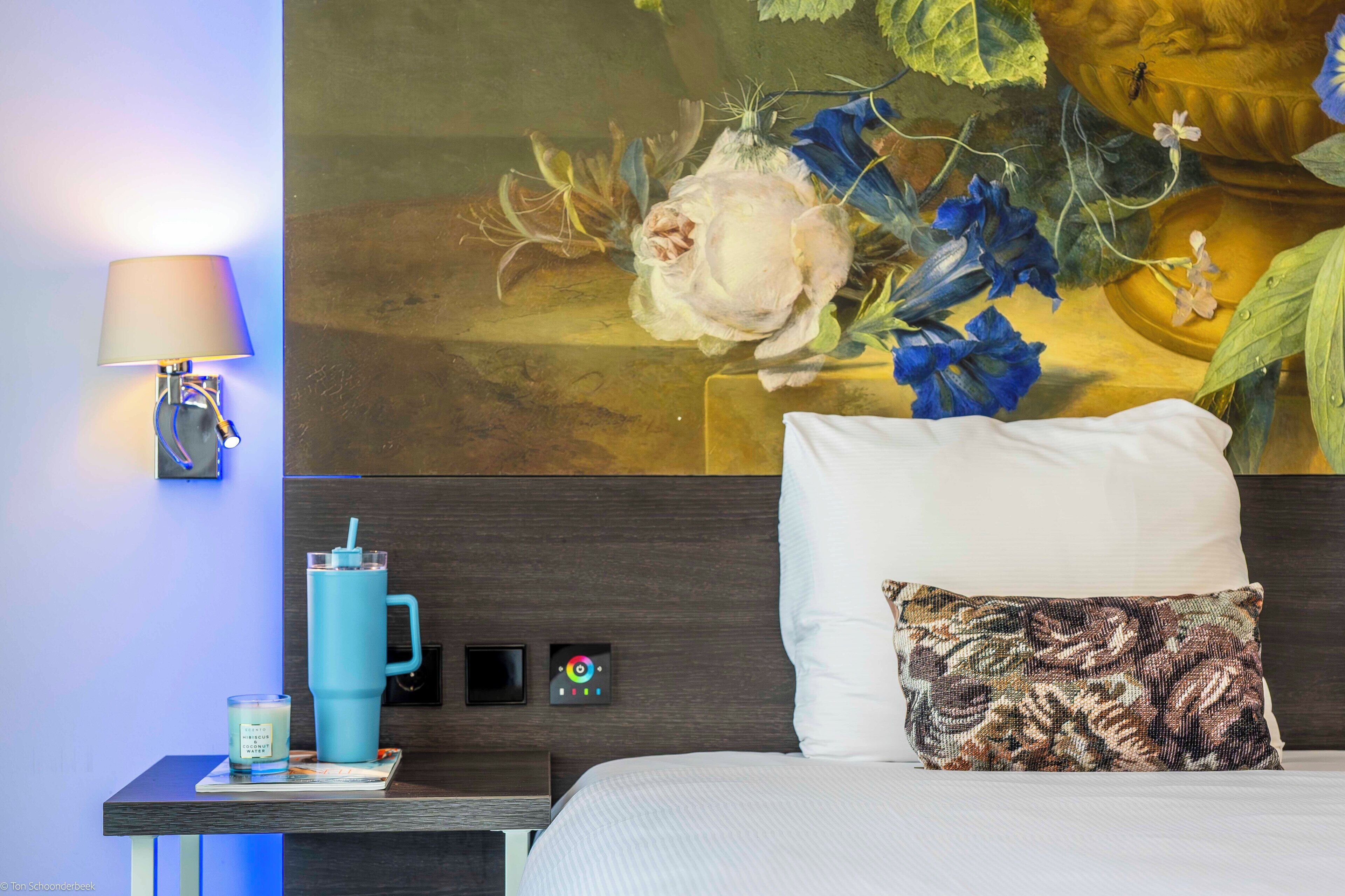 Een hotelkamer met een bed, een nachtkastje met een lamp, een waterfles en een kaars.