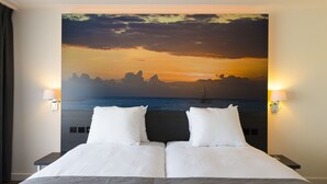 A double bed with a large painting of a sunset over the ocean on the headboard. - Grand Hotel Amstelveen (Amstelveen)