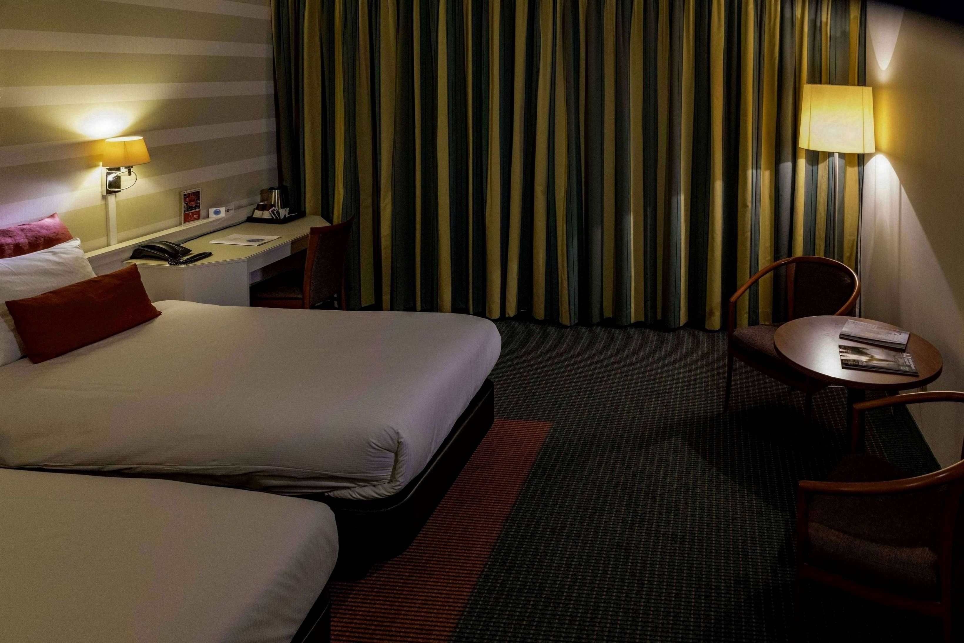 Hotellihuone, jossa on kaksi sänkyä, työpöytä, tuoli ja pieni pöytä.