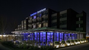 A Grand Hotel Amsterdam building with a modern design, featuring a glass facade and a sign above the entrance. - Grand Hotel Amstelveen (Amstelveen)