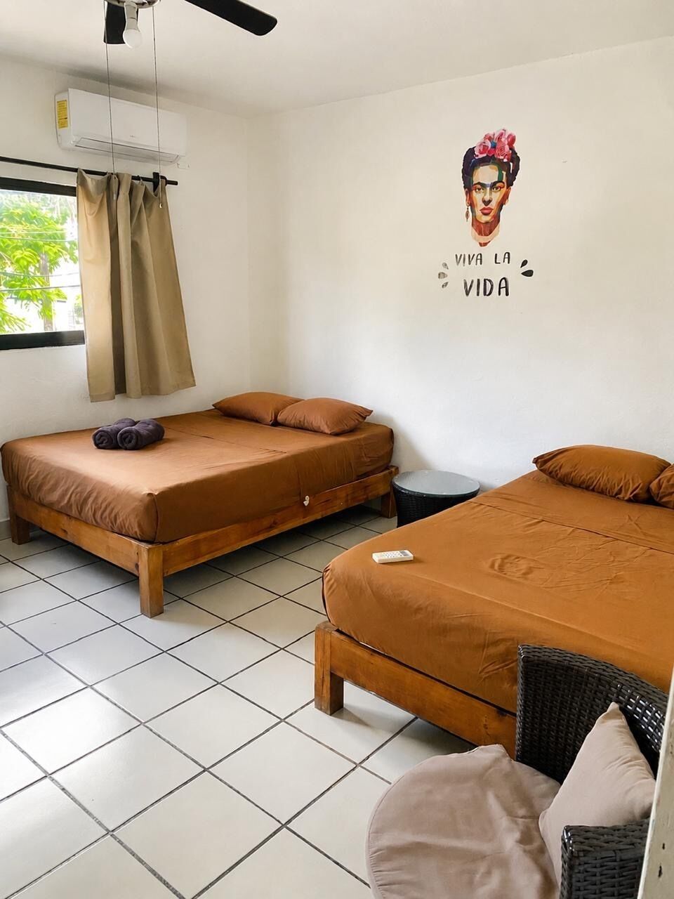 A room with two beds, a ceiling fan, an air conditioning unit, a window with curtains, and a wall with a motivational quote.