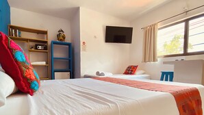 A hotel room with a large bed, a television mounted on the wall, a bookshelf, and a window with curtains.