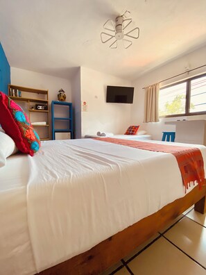 Una habitación de hotel con una cama grande, un televisor montado en la pared, una estantería y una ventana con cortinas.