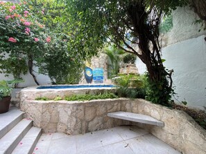 A stone pool with steps leading up to it, surrounded by lush greenery and a sign with travel-related text. - Caribo Cozumel (Cozumel)